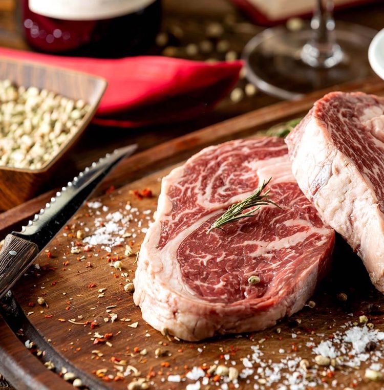 close up raw steak pieces garnished with salt herbs